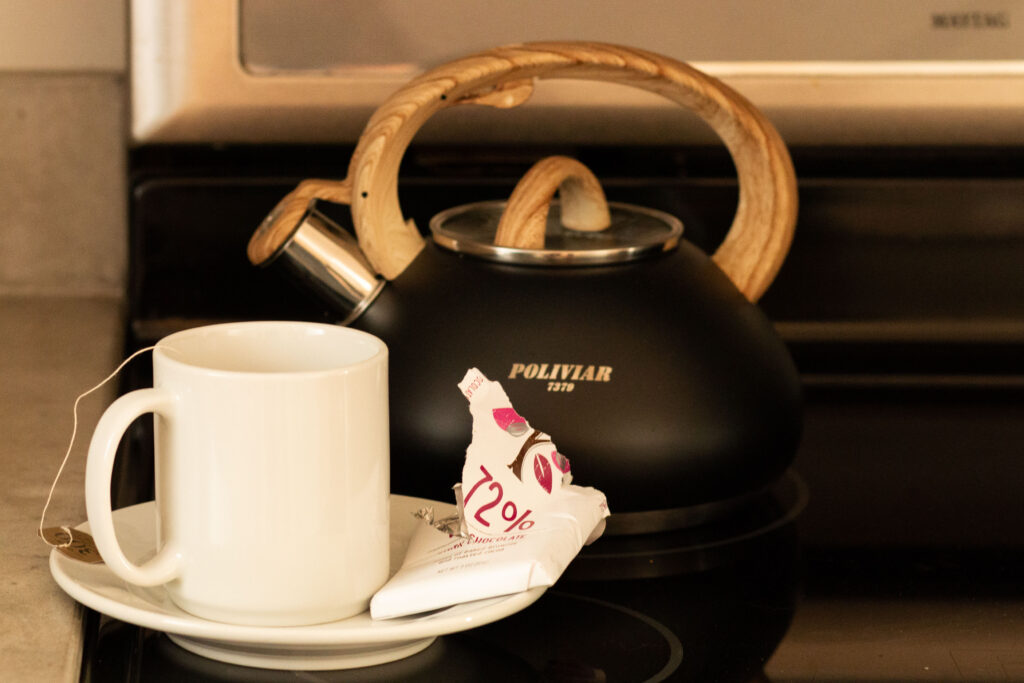 A black tea pot sits in front of a white mug and a bar of Lake Champlain Chocolate on the stove.