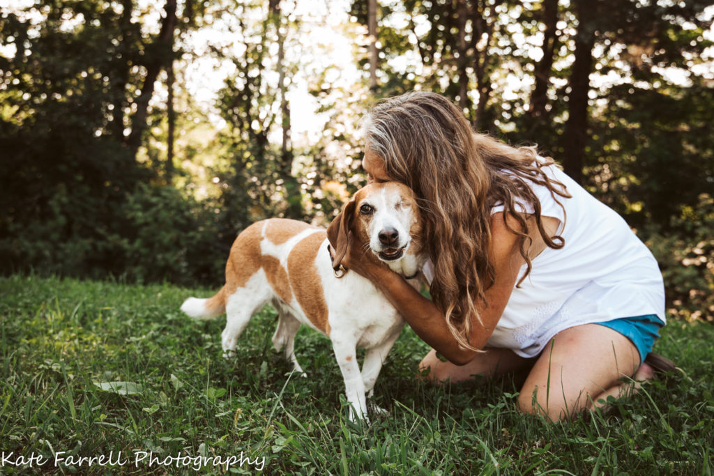 A woman with beautiful long hair hugs a one-eyed beagle. 