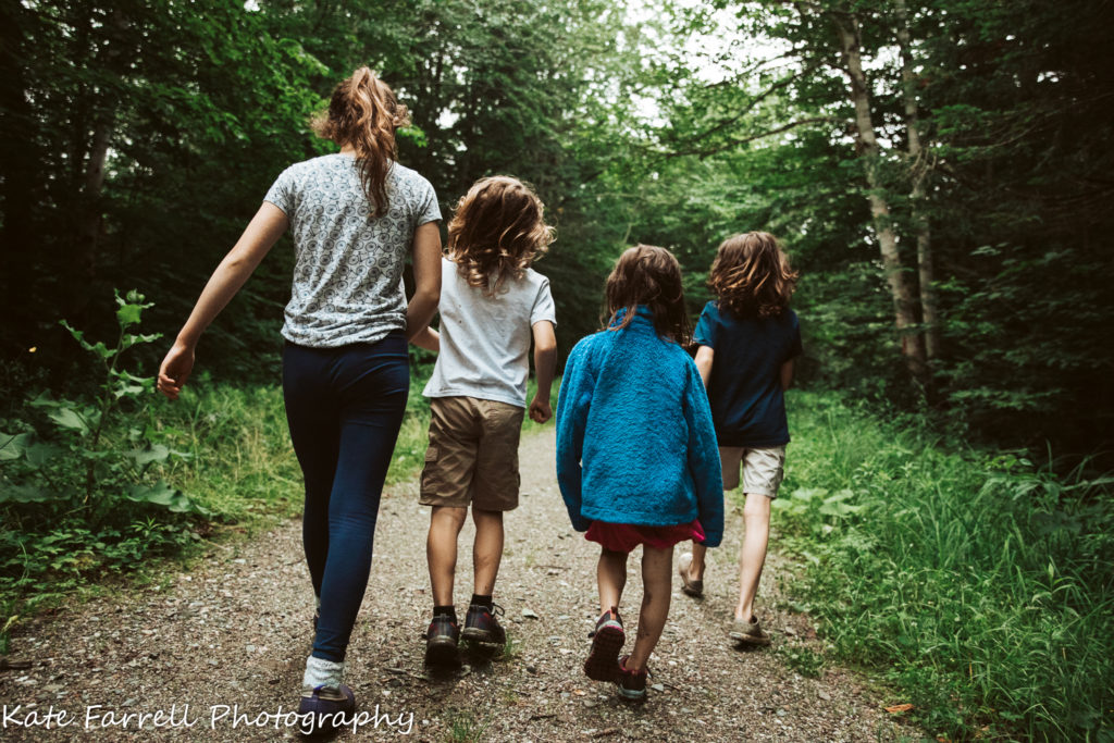 Two girls and two boys walking on a trail in the Vermont woods.