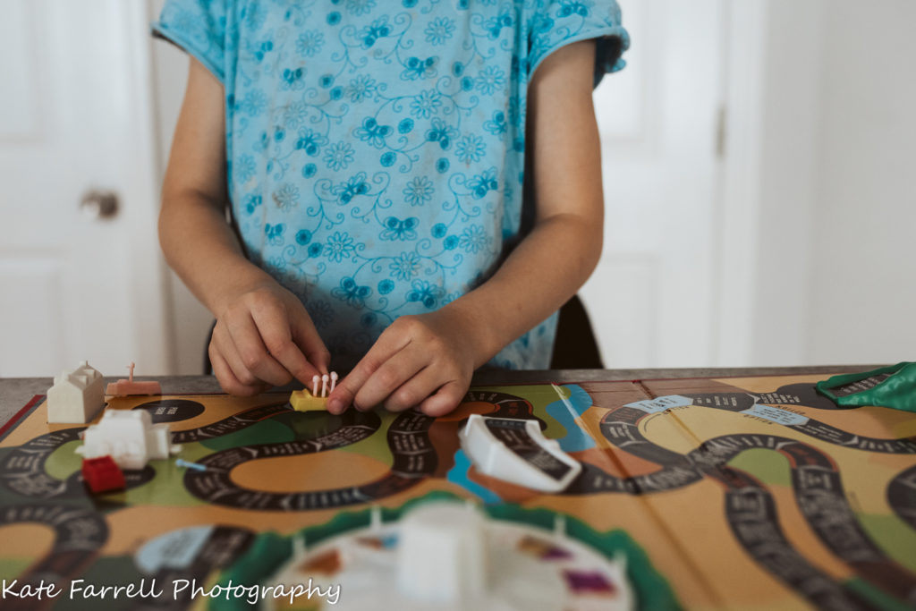 A five year girl's hands play with a Game of Life car on the board.