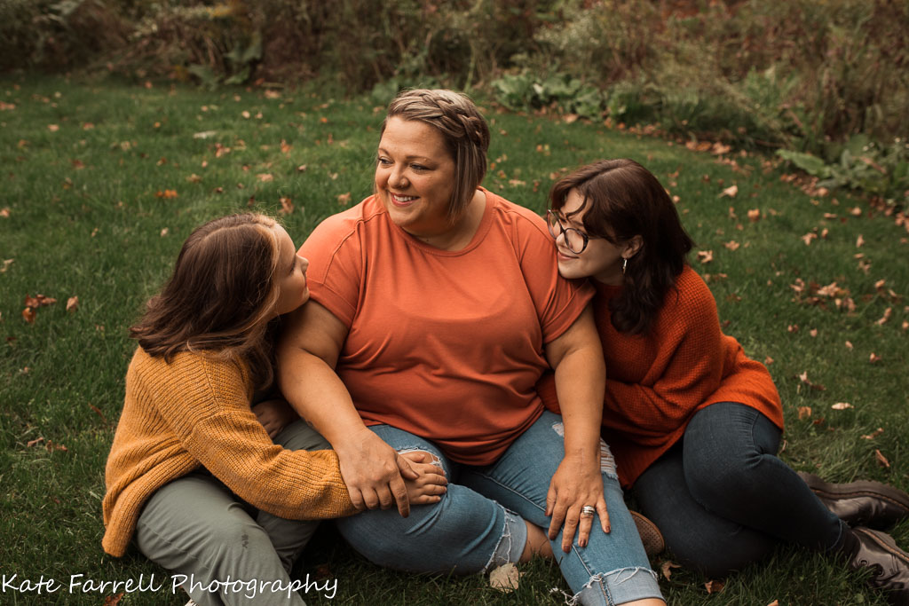 Mother and two daughters sitting and smiling in the grass.