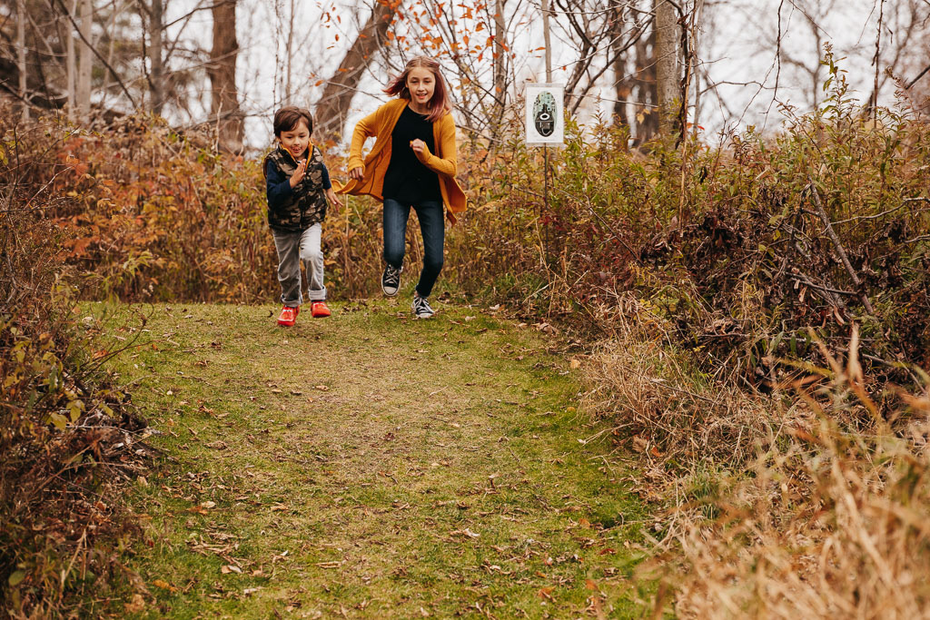 Two kids "racing" down a trail in the fall. An image from one of my Vermont Family Photo Sessions.