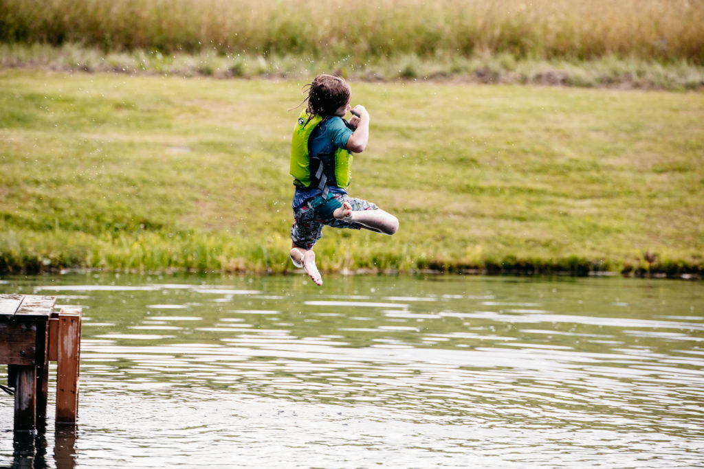 A nine year old boy jumps off a dock into a pond.
