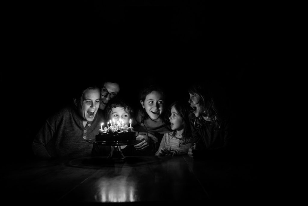 A family gathered around a birthday cake with the candles lit. A 10 year old boy is ready to blow them out.