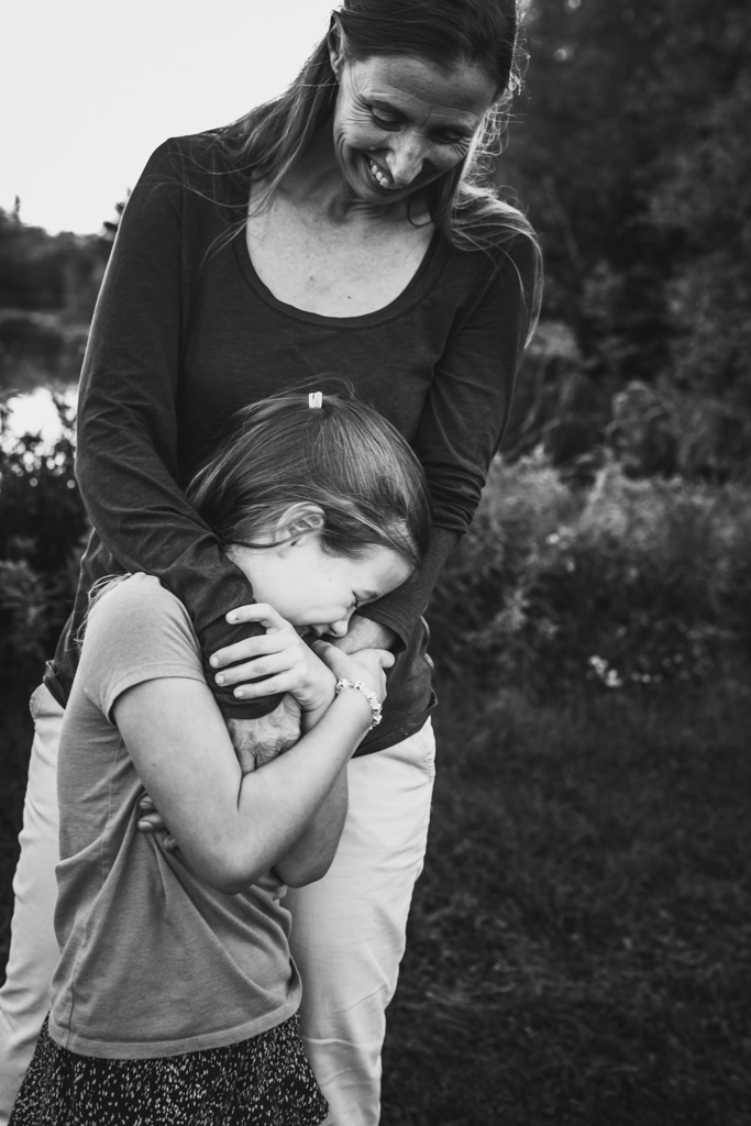 Mother and daughter at a lifestyle family session. T
his is a black and white image. Daughter is leaning in to Mom for a hug.