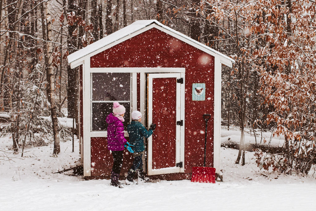 simple family photo of two kids entering a barn red chicken coop while while big snow flakes fall.