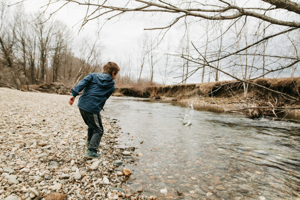 A boy skipping a stone in a shallow river.
