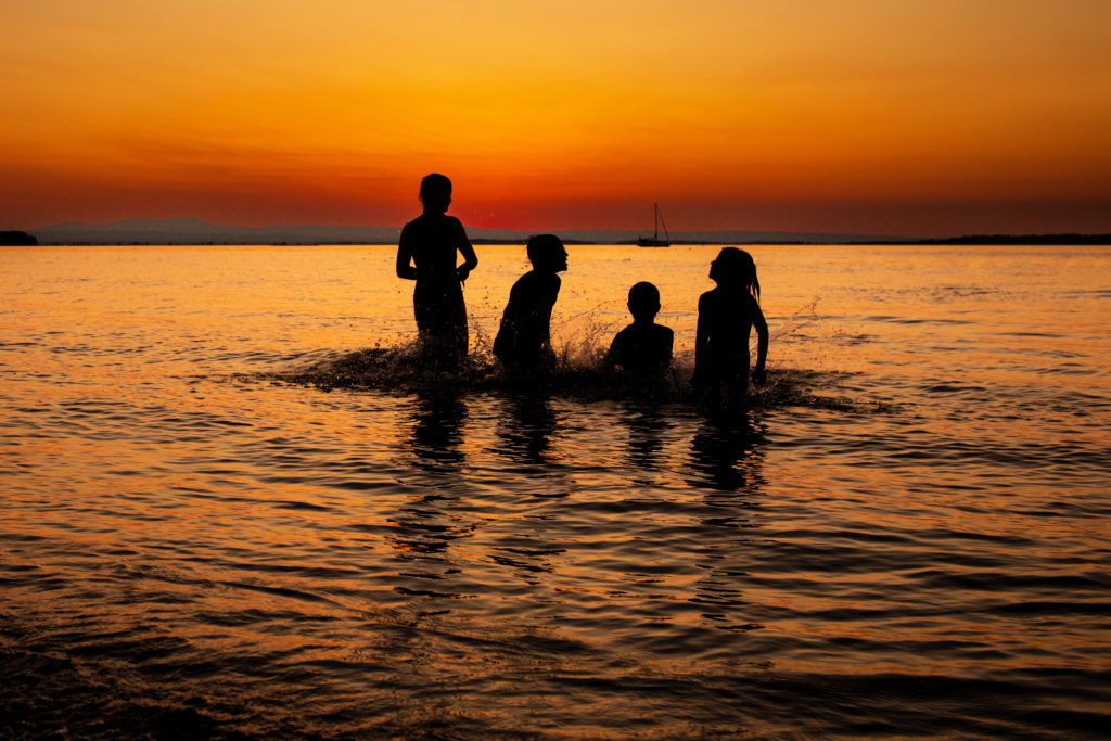 A silhouette of four kids playing in a lake in front of a deep orange sunset.