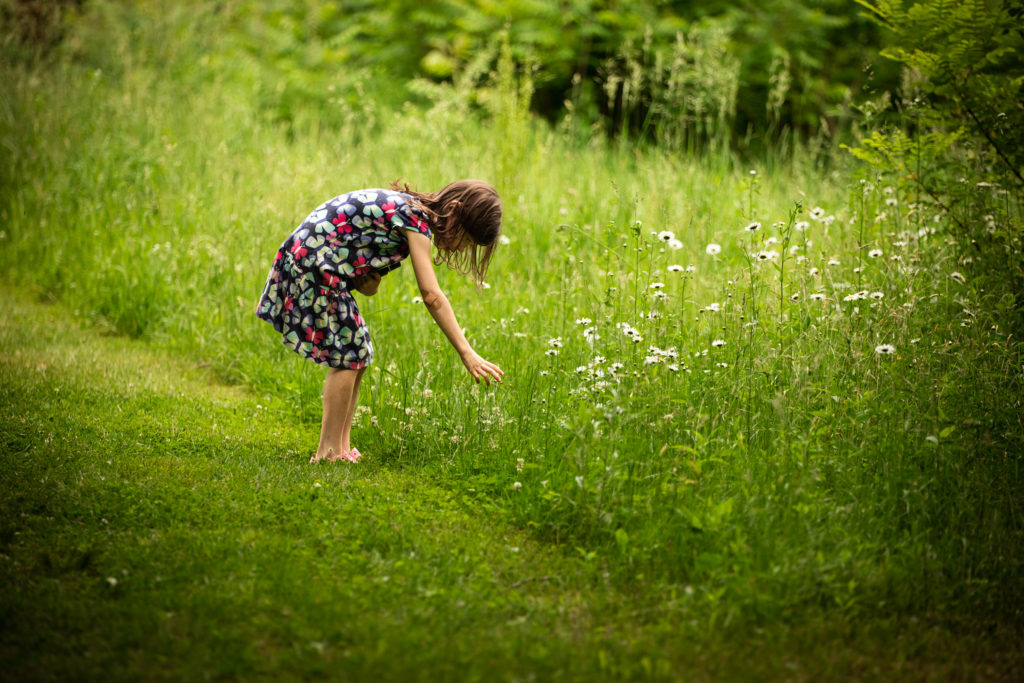 A 6 year old girl bends to pick wildflowers. 