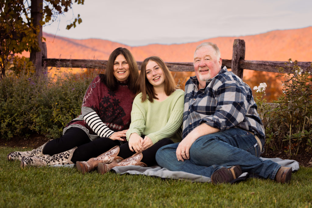 A family of three sits on a blanket in the fall.