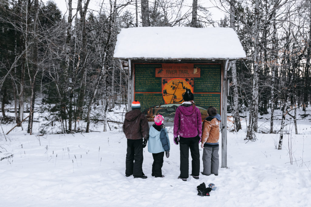 On a cold winter day, four children gather in front of a sign about river ecology.