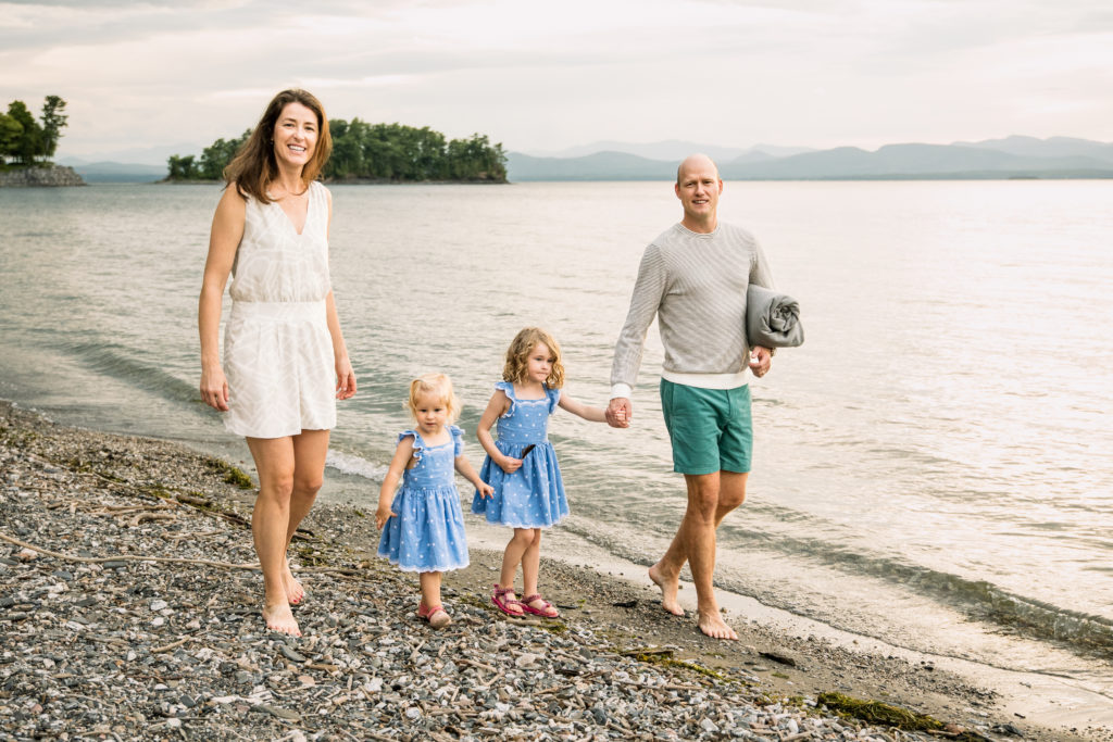 A family of four walks on a rocky beach near Lake Champlain.