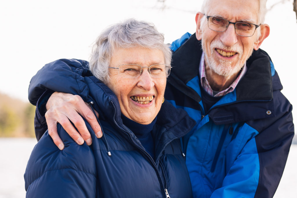 An older couple hugs and smiles on a cold winter day.