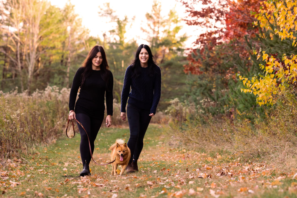 Two women walk a dog in the woods surrounded by beautiful foliage - Vermont Outdoor Family Photography
