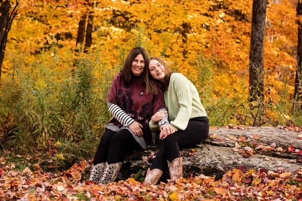Professional Photographer photo of mom and daughter hugging with fall foliage in the background.