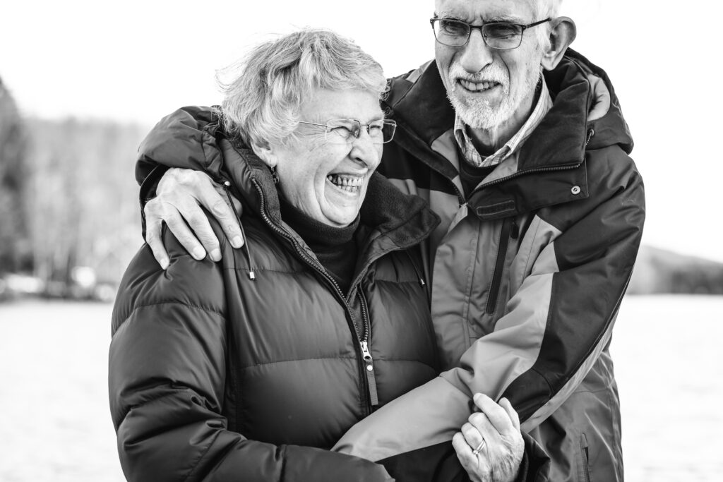 Black and white image of a couple in their 70s embracing and laughing.