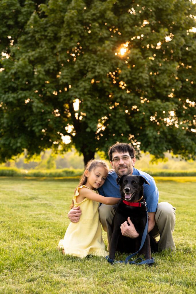 A man and his niece hug a black lab at golden hour -- Vermont dog photography.