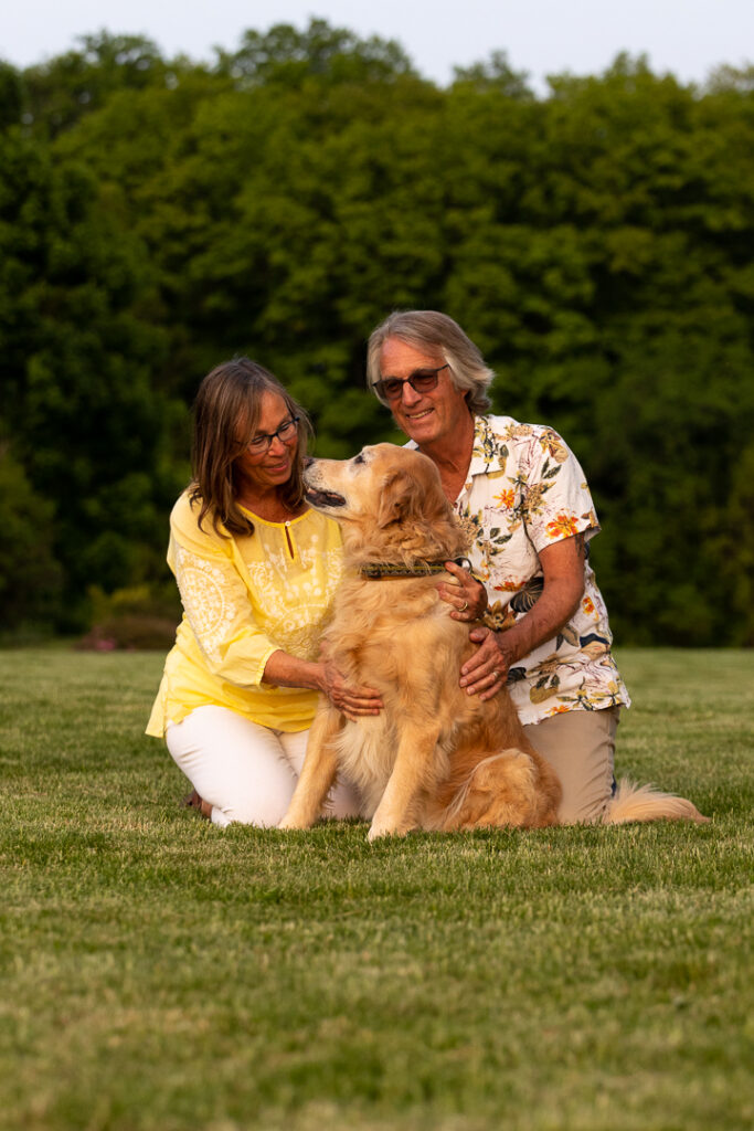 A retired Vermont couple kneel to hug their older Golden Retriever who is looking lovingly into Mom's eyes.