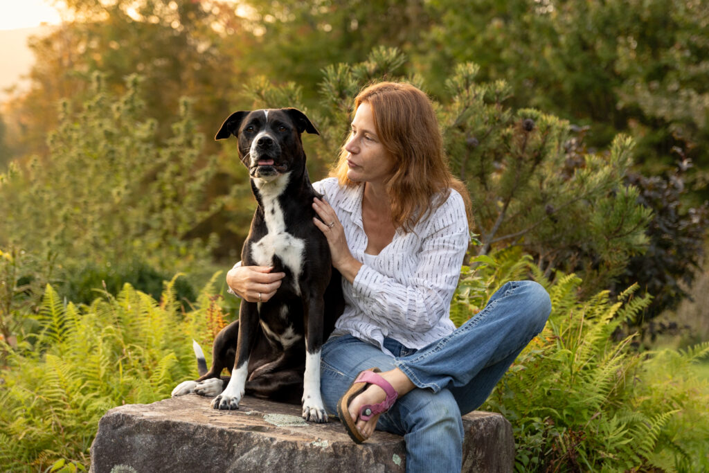 Northern Vermont: a woman sits with her dog with a beautiful sunset behind and off to the side.