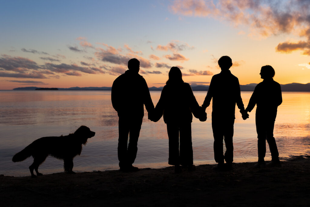 Silhouette of a family of four and their dog on the shore of Lake Champlain.