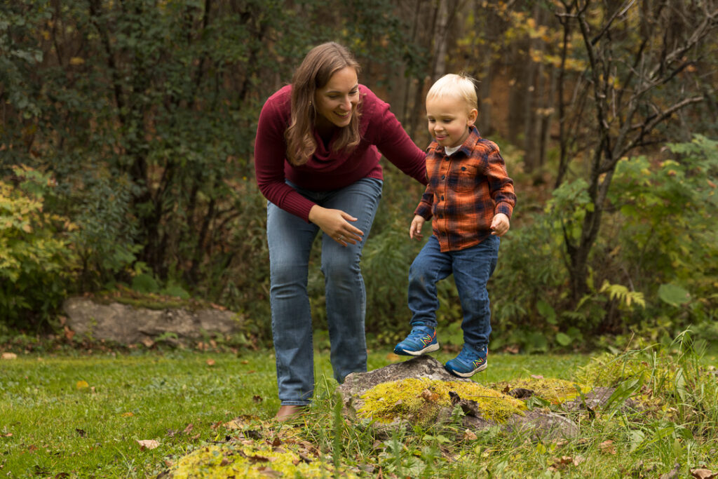 Mom encouraging her toddler son as he climbs on rocks during a fall Vermont family photo session.