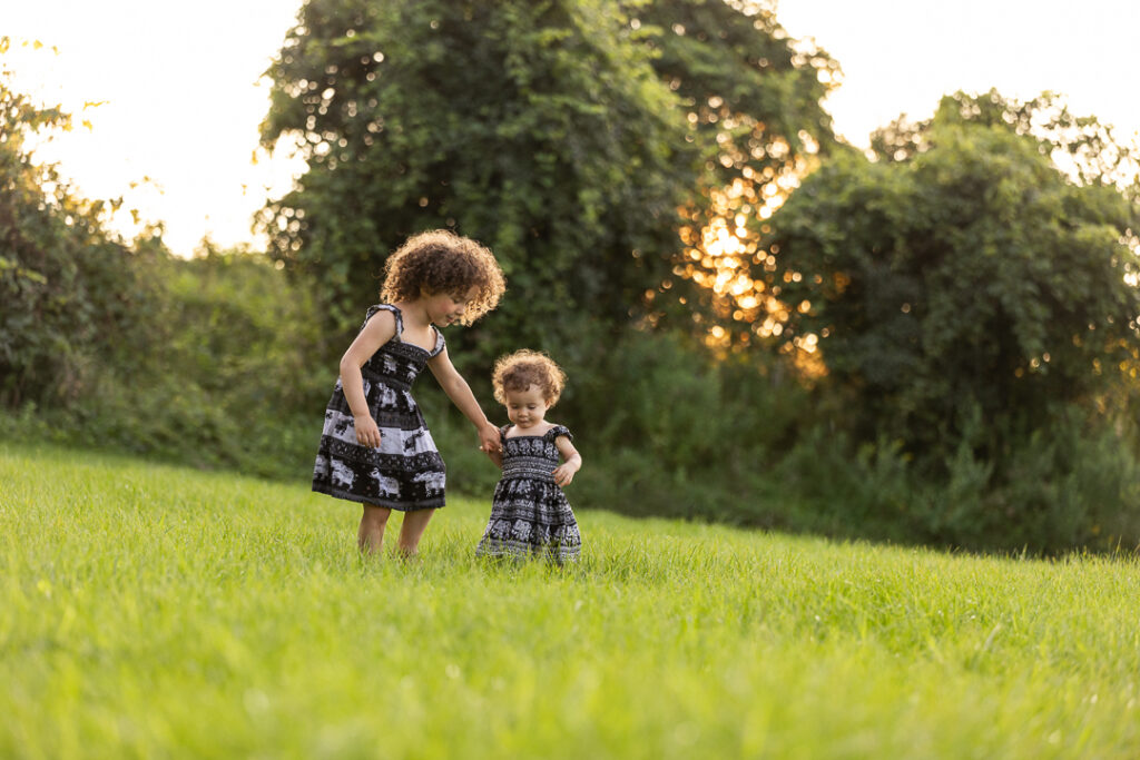 Two young girls walk in a field during a Williston Vermont family photo session.
